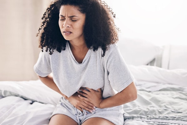 Abdomen pain, period and black woman in bed with abdominal cramps, menstruation and stomach ache. Health, medical emergency and girl with digestion problem, pms crisis and endometriosis in bedroom